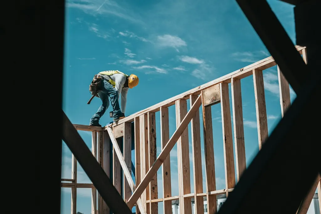 A framer working on top of a wall frame against the sky, seen from below