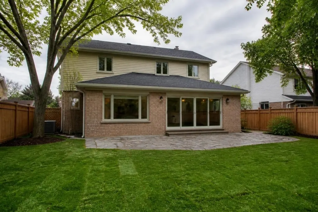 The back of a two-storey brick house with a single-storey addition that has large windows and patio doors facing the lawn